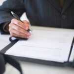 Close-up of a hand signing documents with a pen, symbolizing an important business contract.